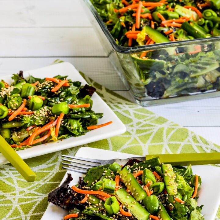 Asian Green Salad with Soy-Sesame Dressing shown on two serving plates with salad bowl in back.