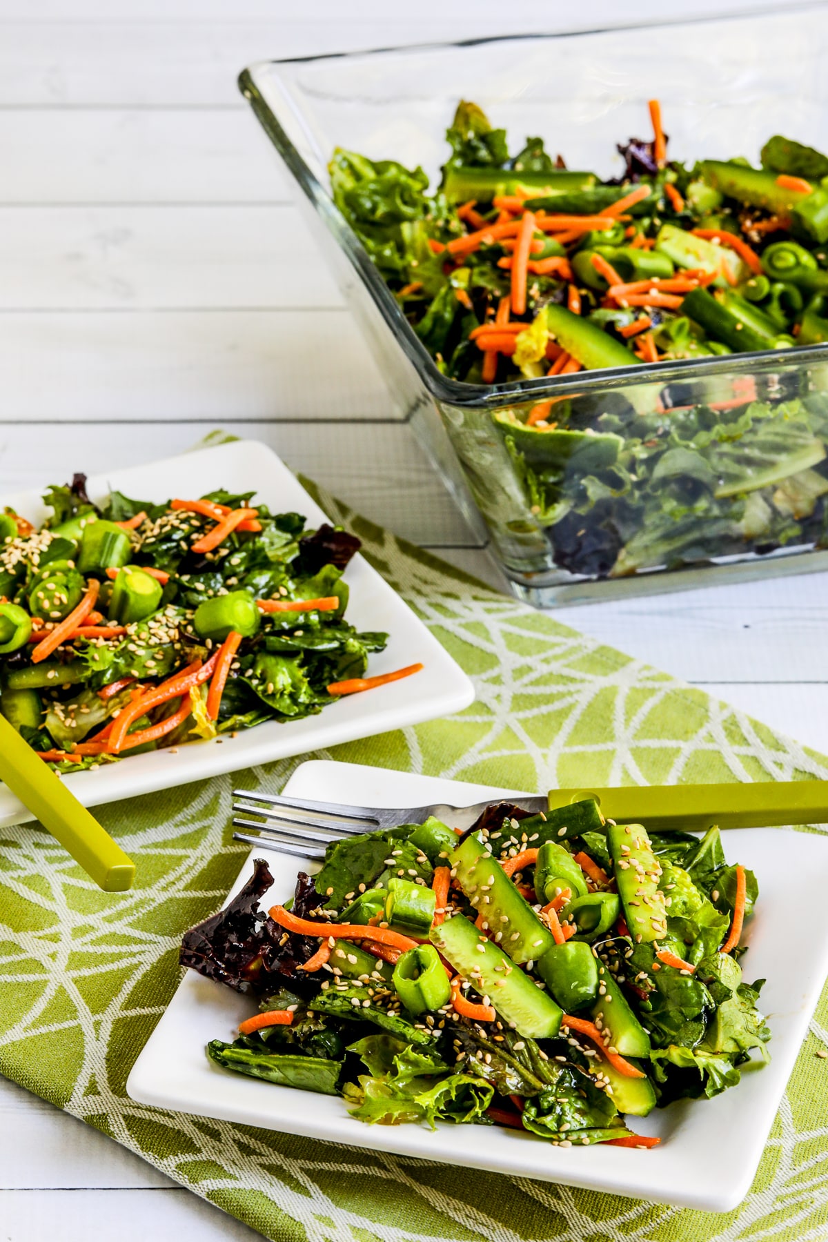 Asian Green Salad with Soy-Sesame Dressing shown on two serving plates with salad bowl in back.