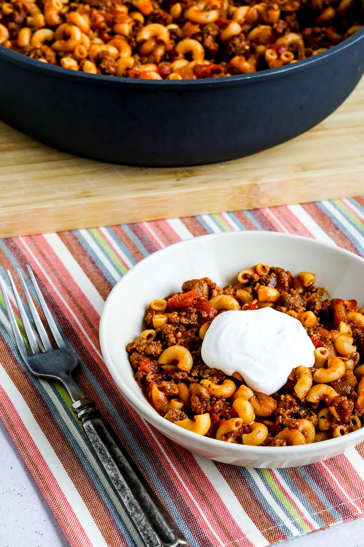 Better-than-Mom's Hamburger Goulash showing one serving in bowl with pan of Goulash in back.