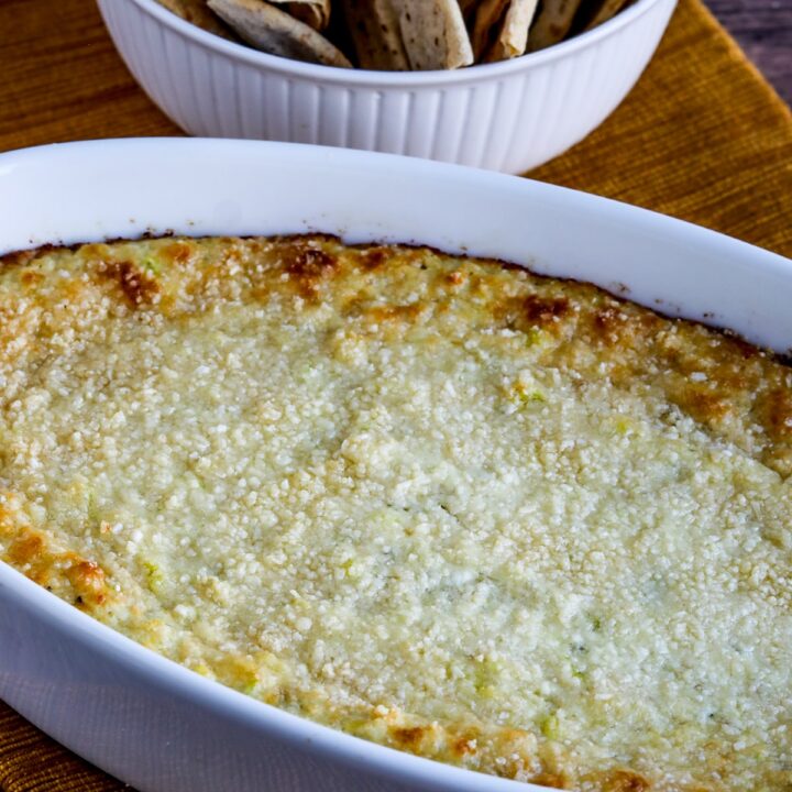 Hot Artichoke Dip (with Peperoncini) shown in bowl with toasted low-carb pita bread in back.