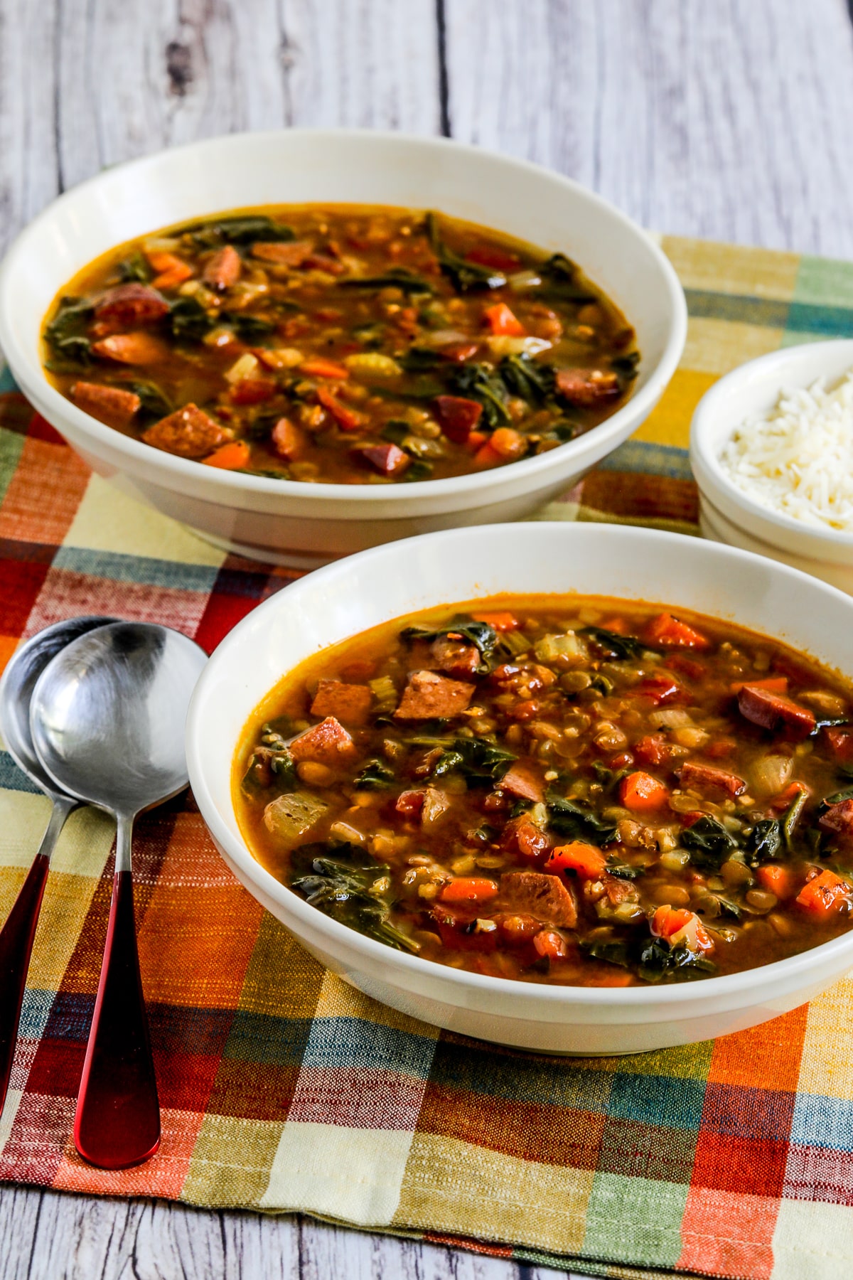 Sausage Lentil Soup with Spinach in two bowls with spoons and Parmesan.