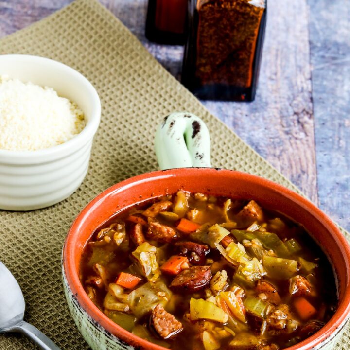 Sausage and Cabbage Soup shown in bowl with spoon, with Parmesan and salt-pepper shakers.