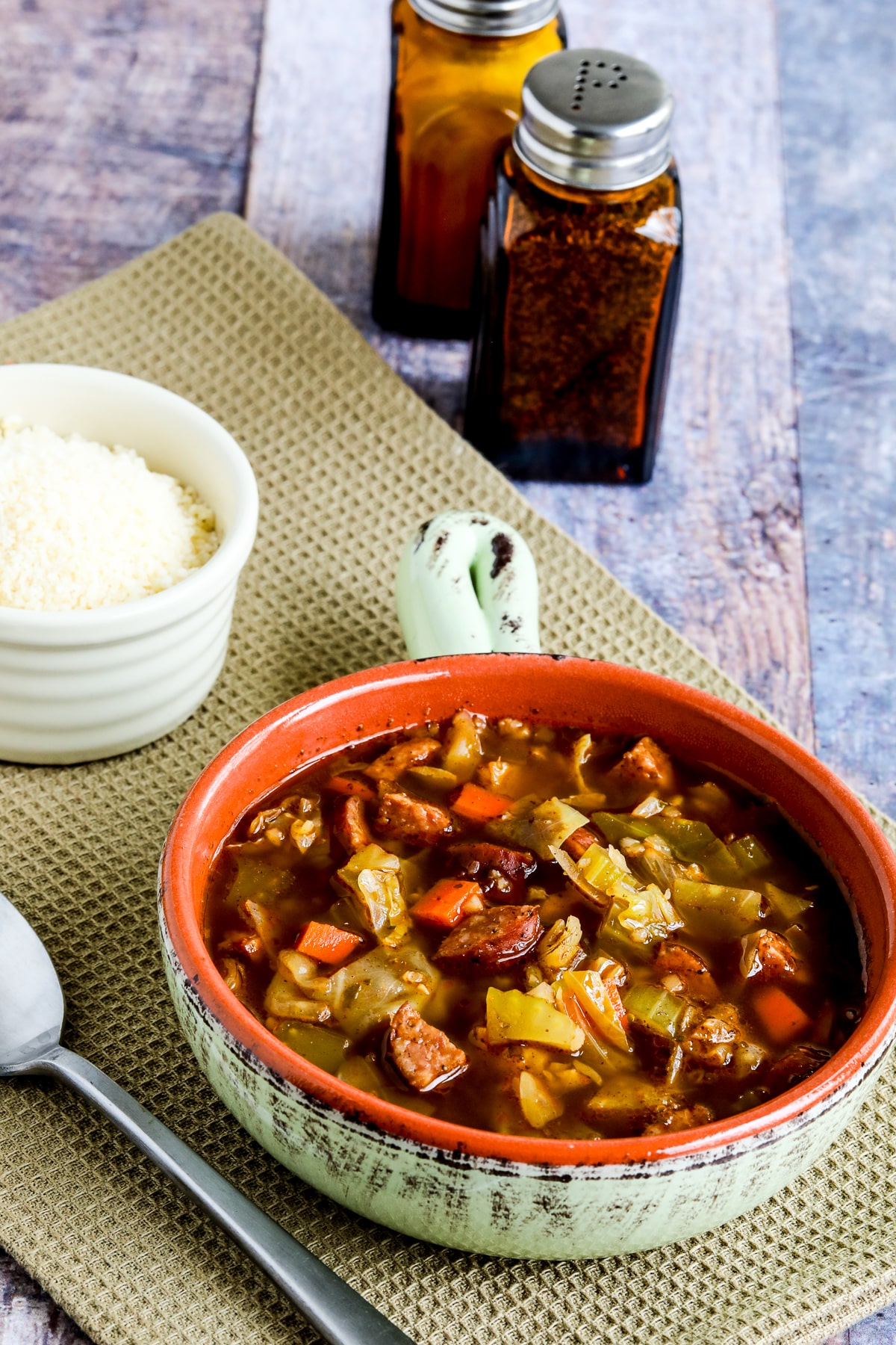 Sausage and Cabbage Soup shown in bowl with spoon, with Parmesan and salt-pepper shakers.