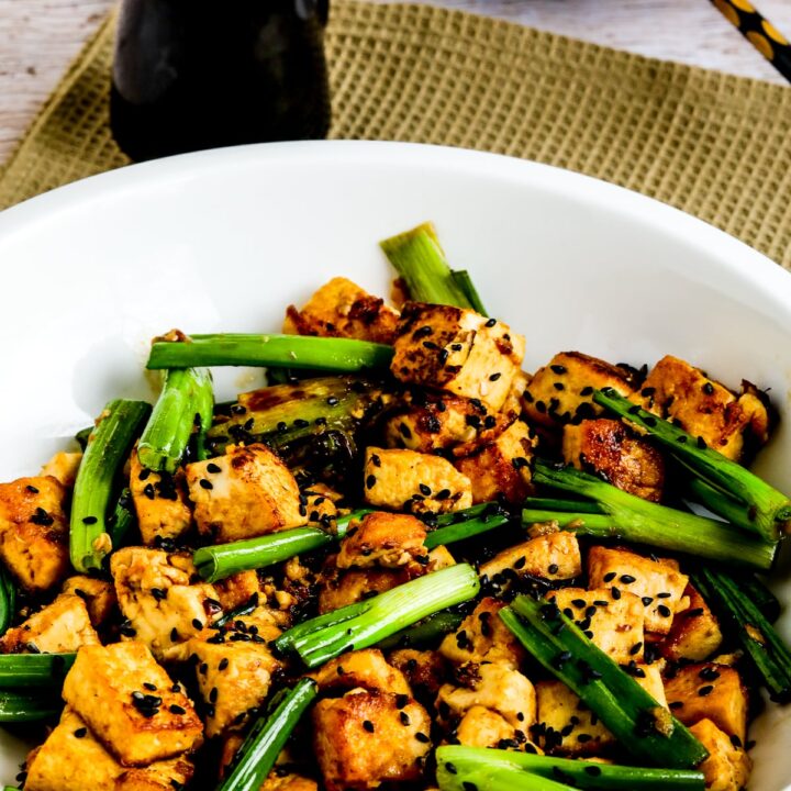 Stir-Fried Tofu with Ginger and Soy Sauce shown in serving dish with soy sauce container and chopsticks on plate.