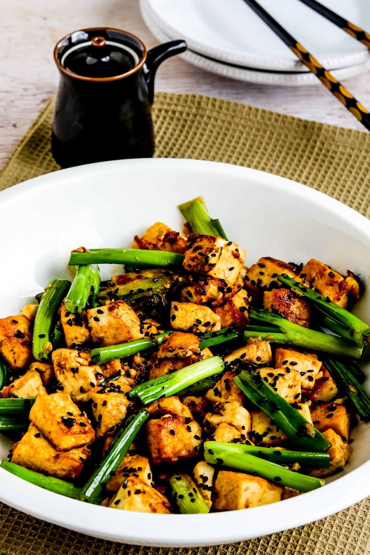 Stir-Fried Tofu with Ginger and Soy Sauce shown in serving dish with soy sauce container and chopsticks on plate.