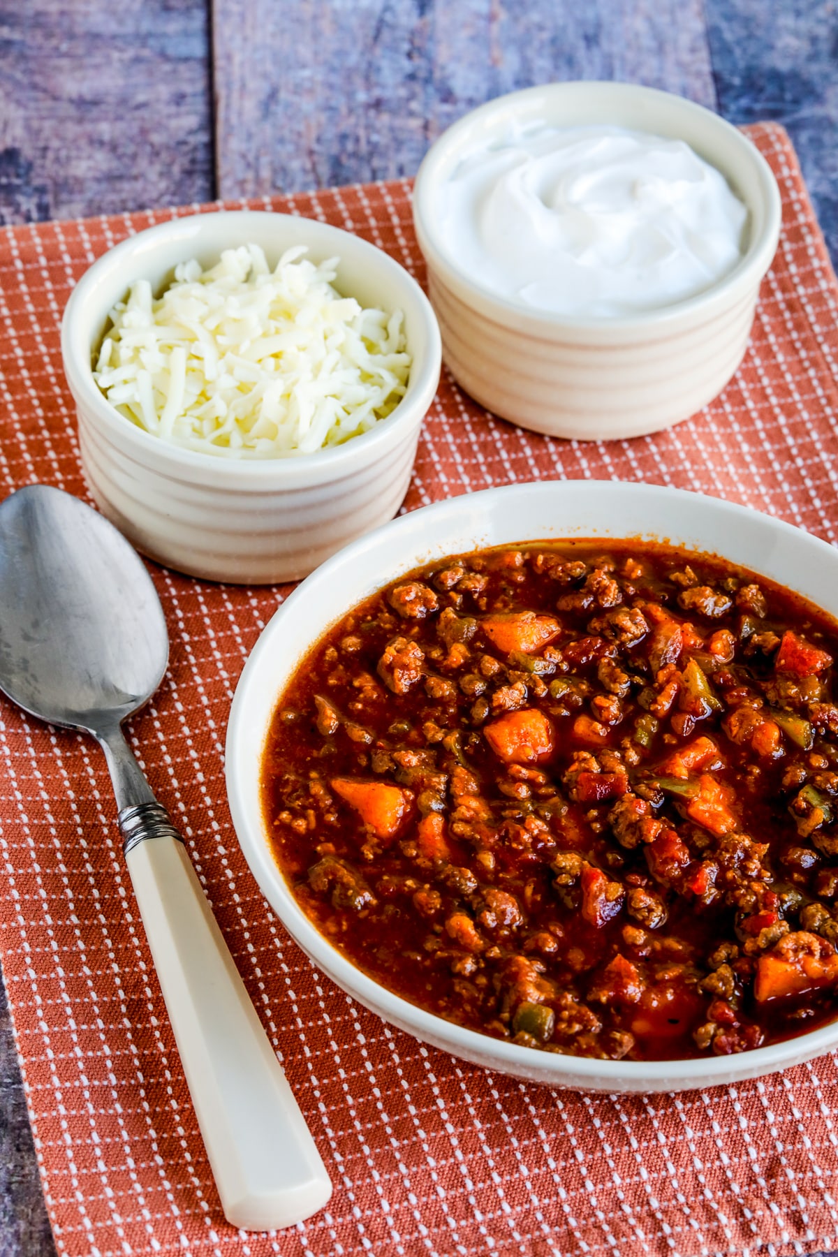 Turkey Sweet Potato Chili showing turkey chili in bowl with spoon and cheese and sour cream in back.