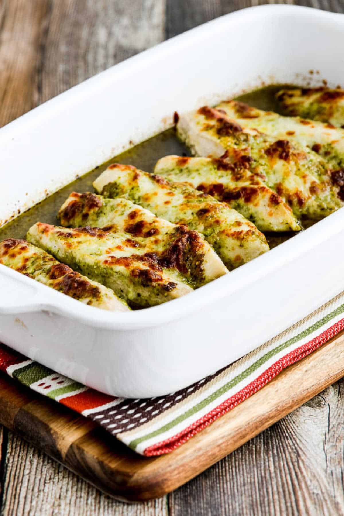 Easy Baked Pesto Chicken in baking dish on striped napkin and cutting board