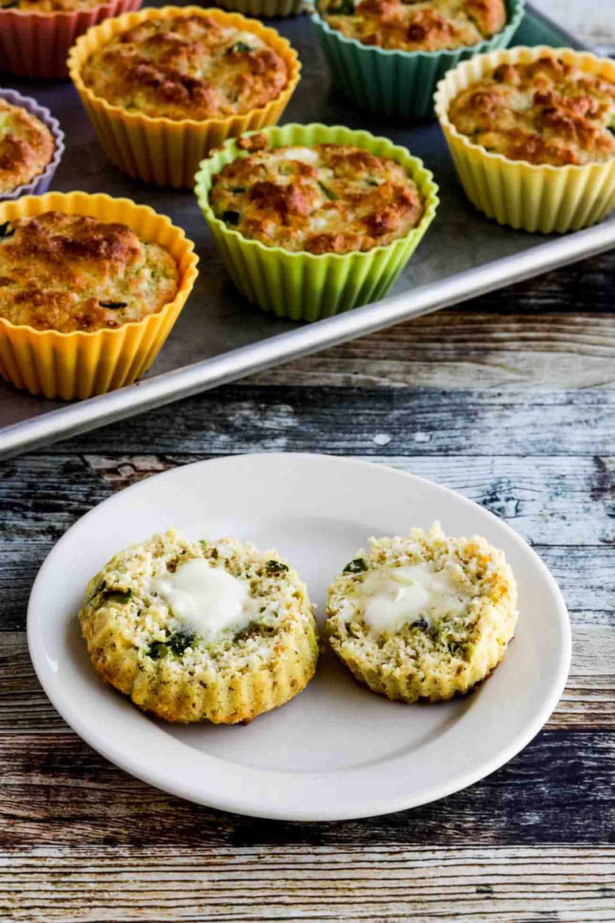 Flourless Breakfast Muffins with Zucchini and Feta shown in baking cups with one muffin split and served with butter