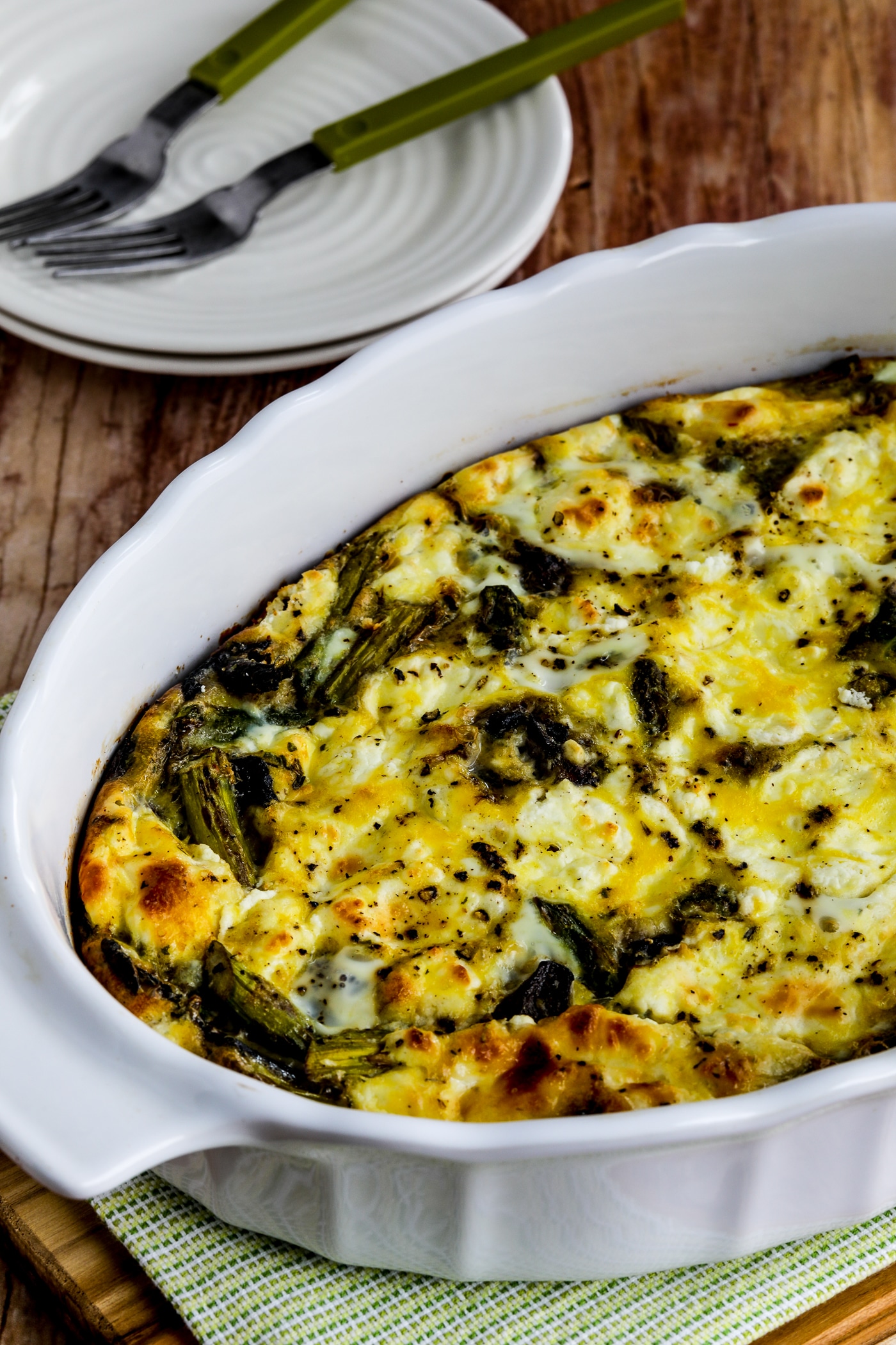 Asparagus, Mushroom, and Goat Cheese Breakfast Casserole shown in baking dish with plates, forks, and napkin