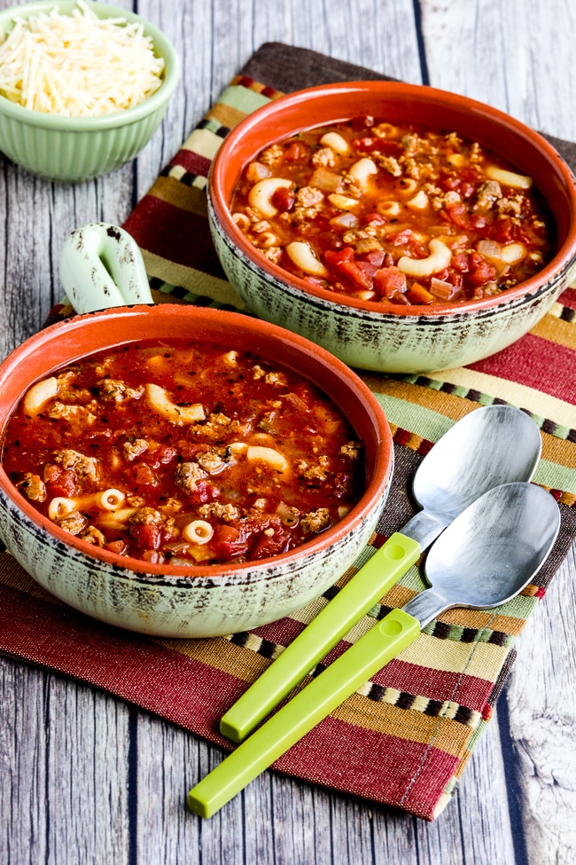 Italian Sausage, Tomato, and Pesto Soup shown in two bowls with Parmesan on the side.