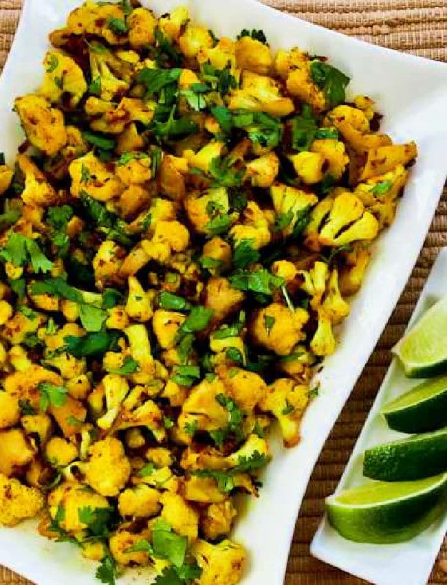 Curried Cauliflower shown on serving plate with limes.