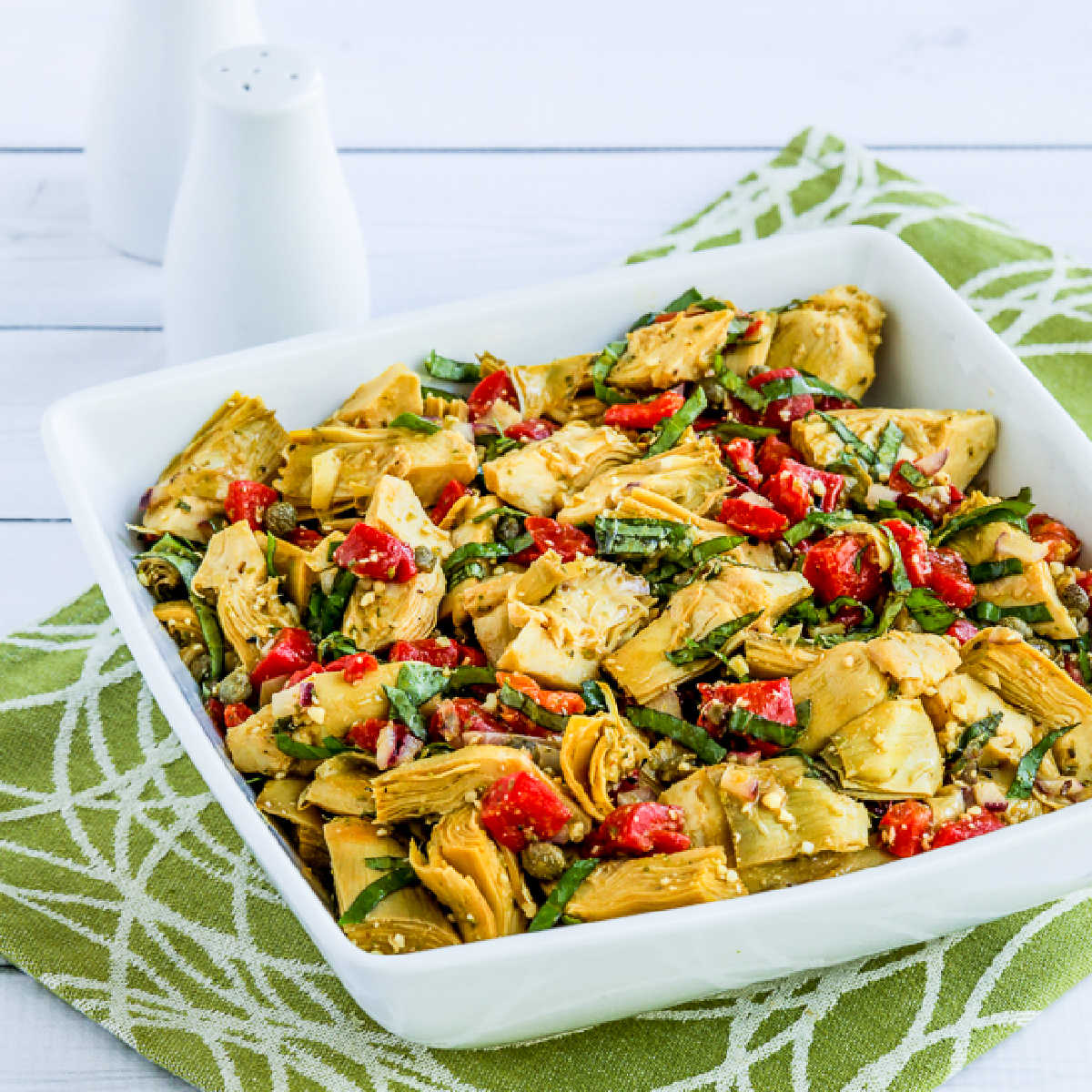 Square image of Artichoke Heart Salad in square bowl on green-white napkin.