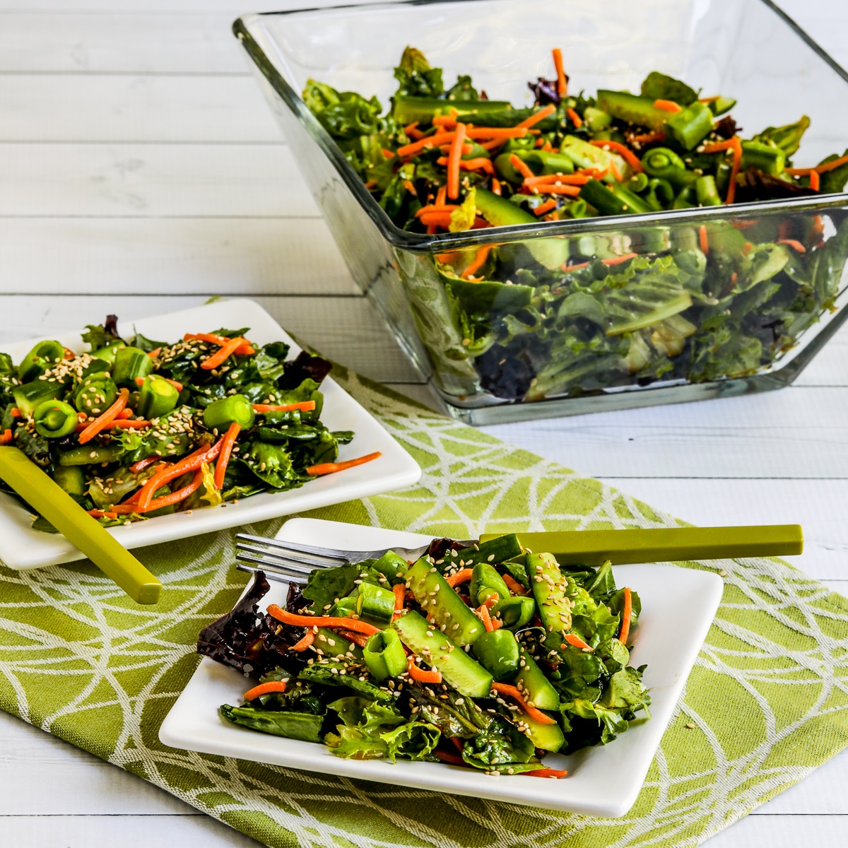 Square image for Asian Green Salad with Soy-Sesame Dressing with two serving on small plates and salad bowl in back.