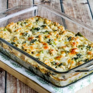 Square image of Chicken Broccoli Alfredo Casserole in baking dish on napkin and cutting board.