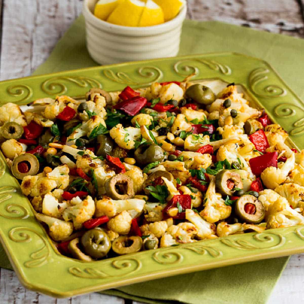 square image of Roasted Cauliflower with Red Peppers, Green Olives, and Pine Nuts shown on green serving plate