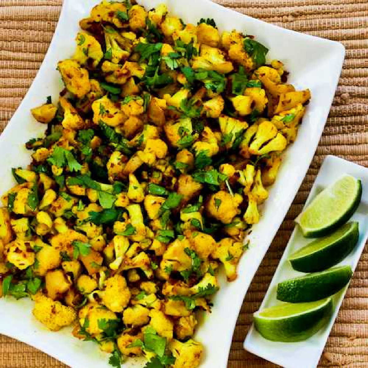 Square image of Curried Cauliflower (Gobi Taktakin) shown on serving platter with limes.