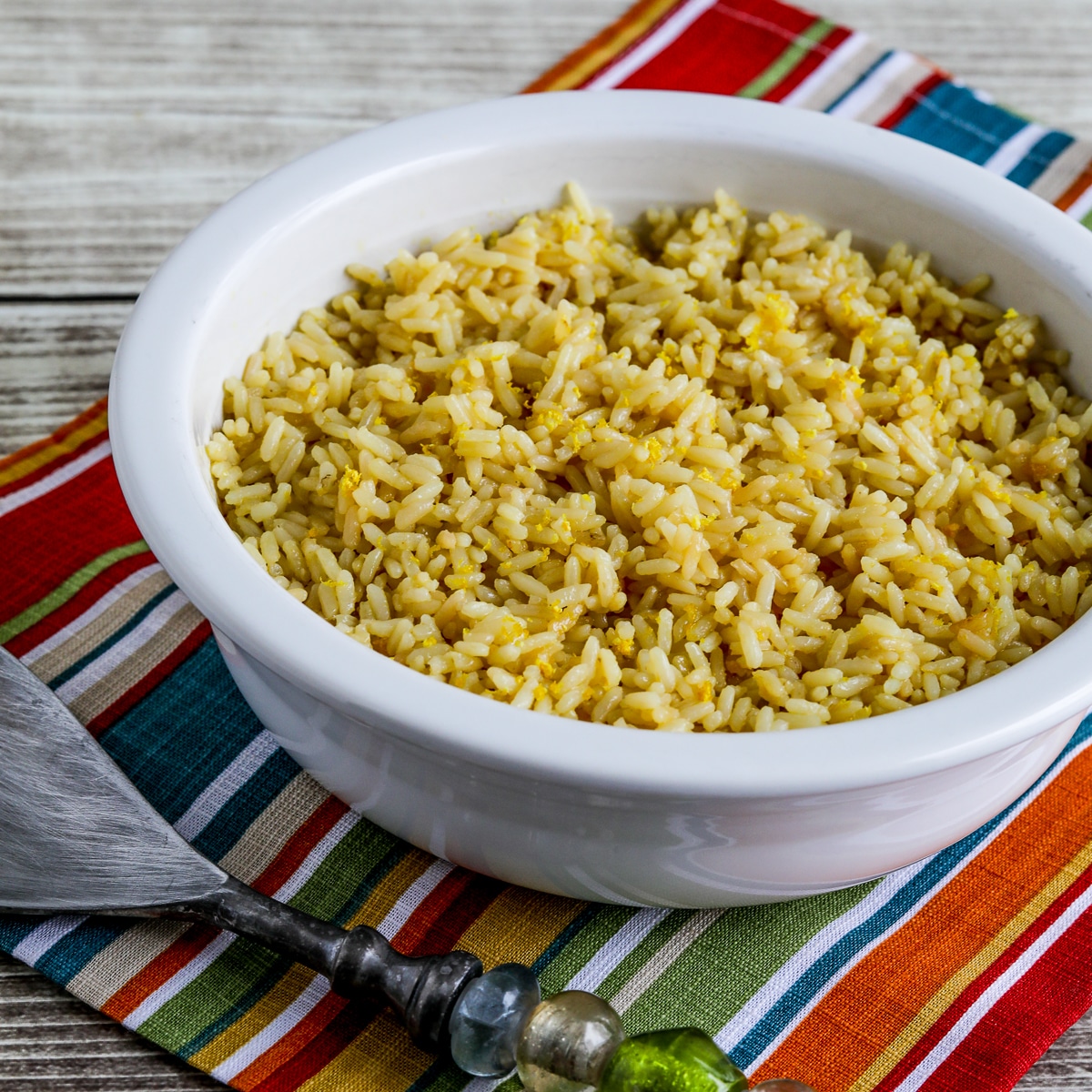 Square image of Greek Lemon Rice recipe shown in serving bowl with serving spoon.