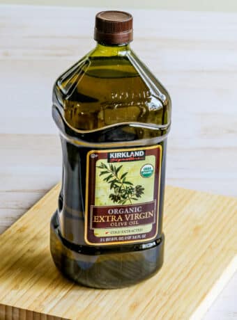 Kirkland Organic Extra-Virgin Olive Oil square image of olive oil bottle on cutting board.