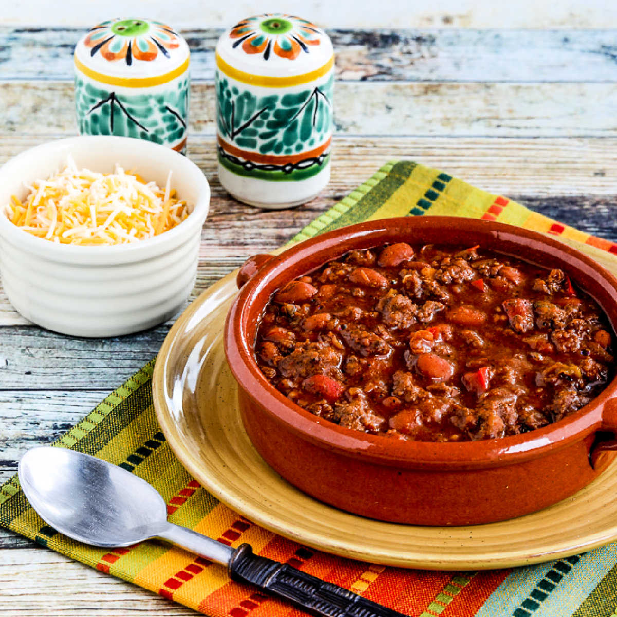 Square image of Slow Cooker Beef and Refried Bean Chili shown in serving bowl on plate.