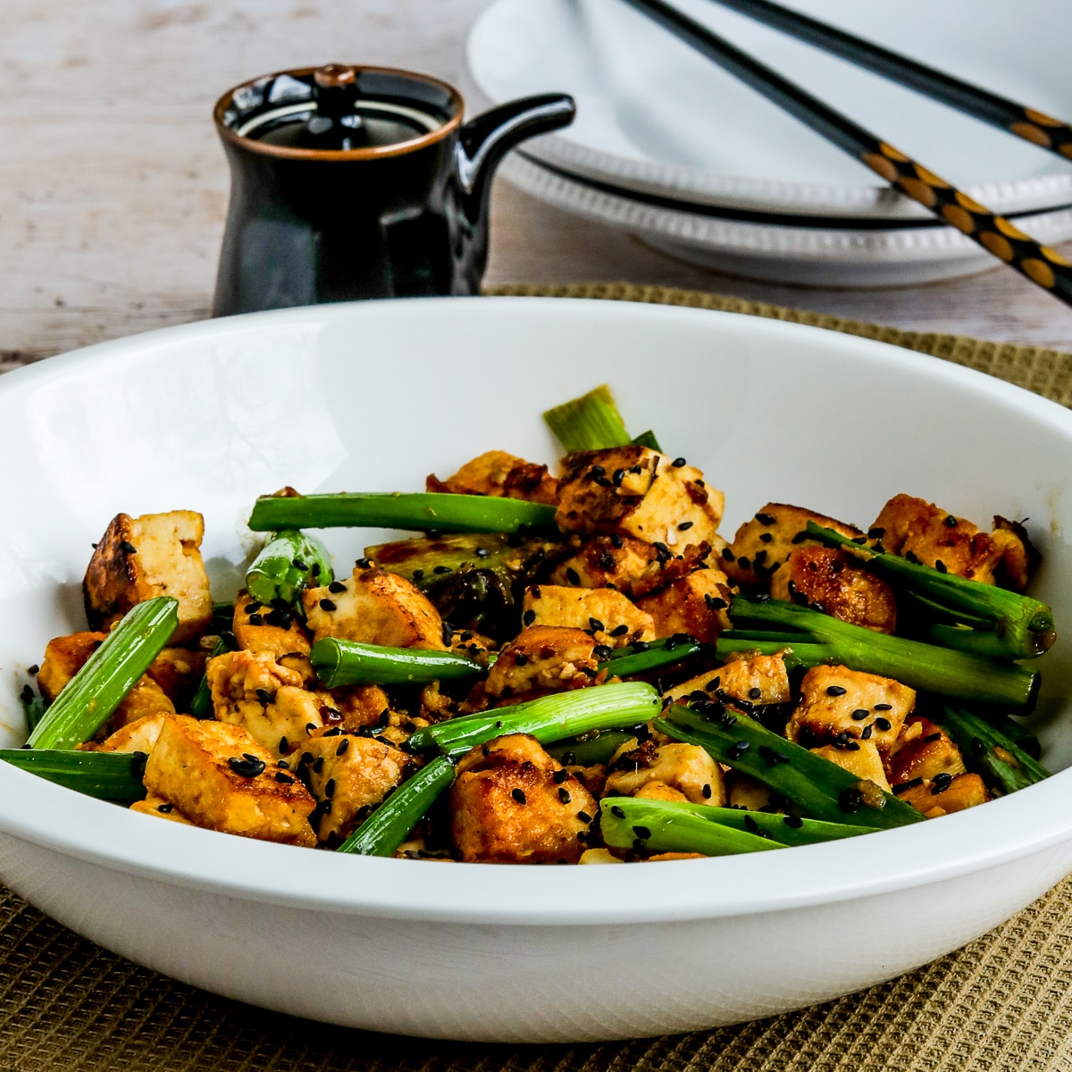 Square image for Stir-Fried Tofu with Ginger And Soy Sauce shown in serving bowl with soy sauce dispenser and chopsticks in back.