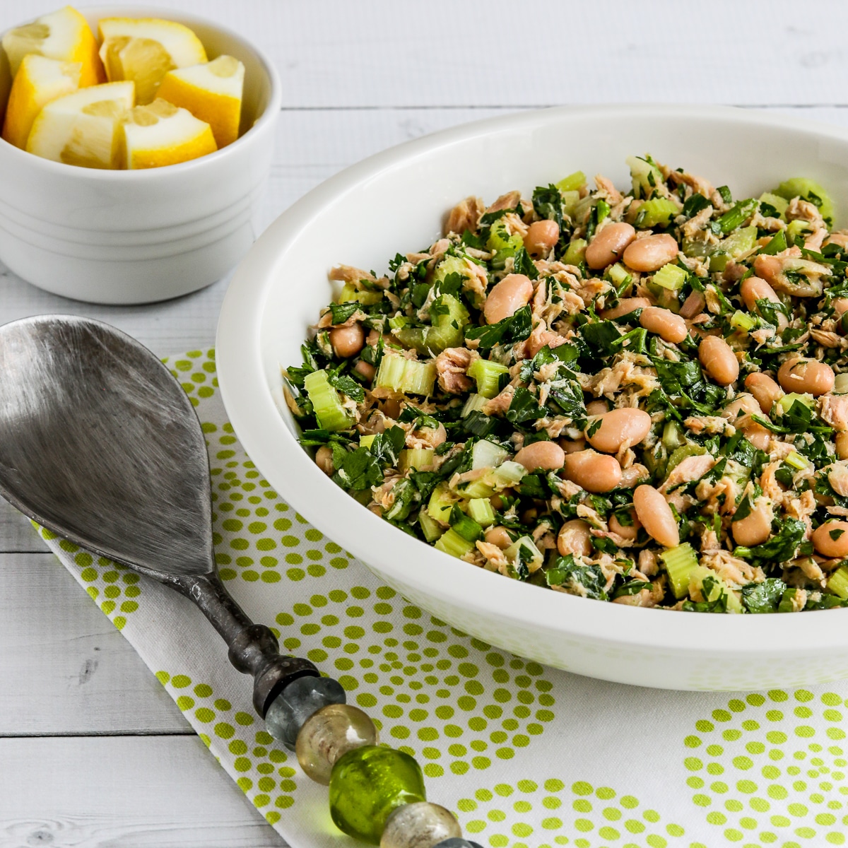 Square image for Tuna White Bean Salad in serving bowl with fork and lemon wedges.