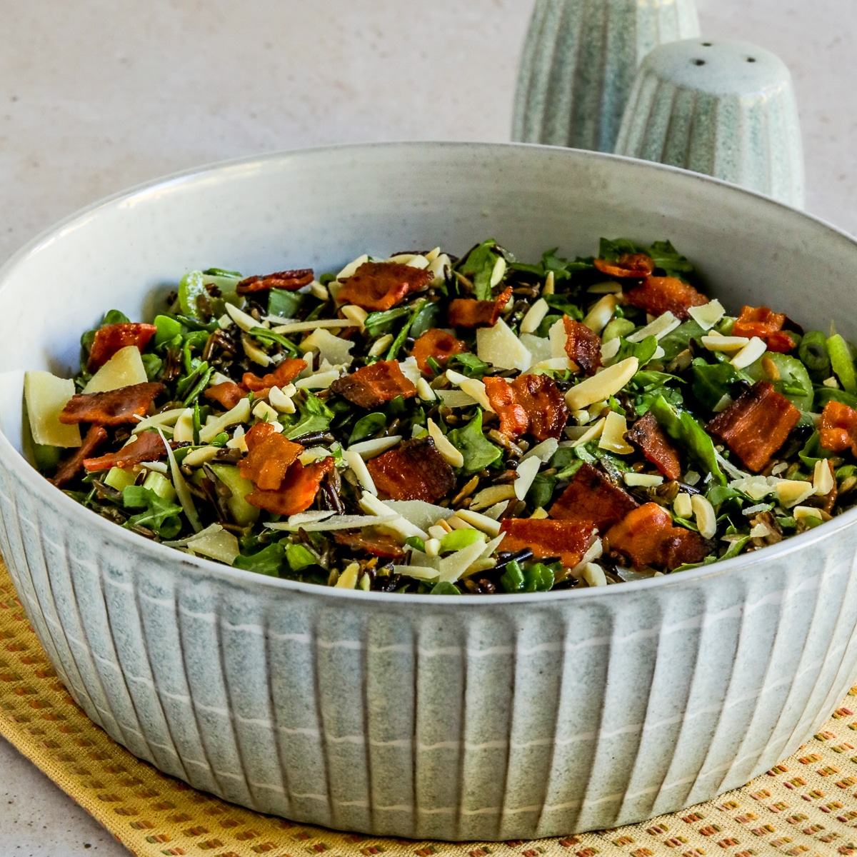 Square image for Wild Rice Salad with Bacon and Arugula shown in bowl with salt-pepper in back.