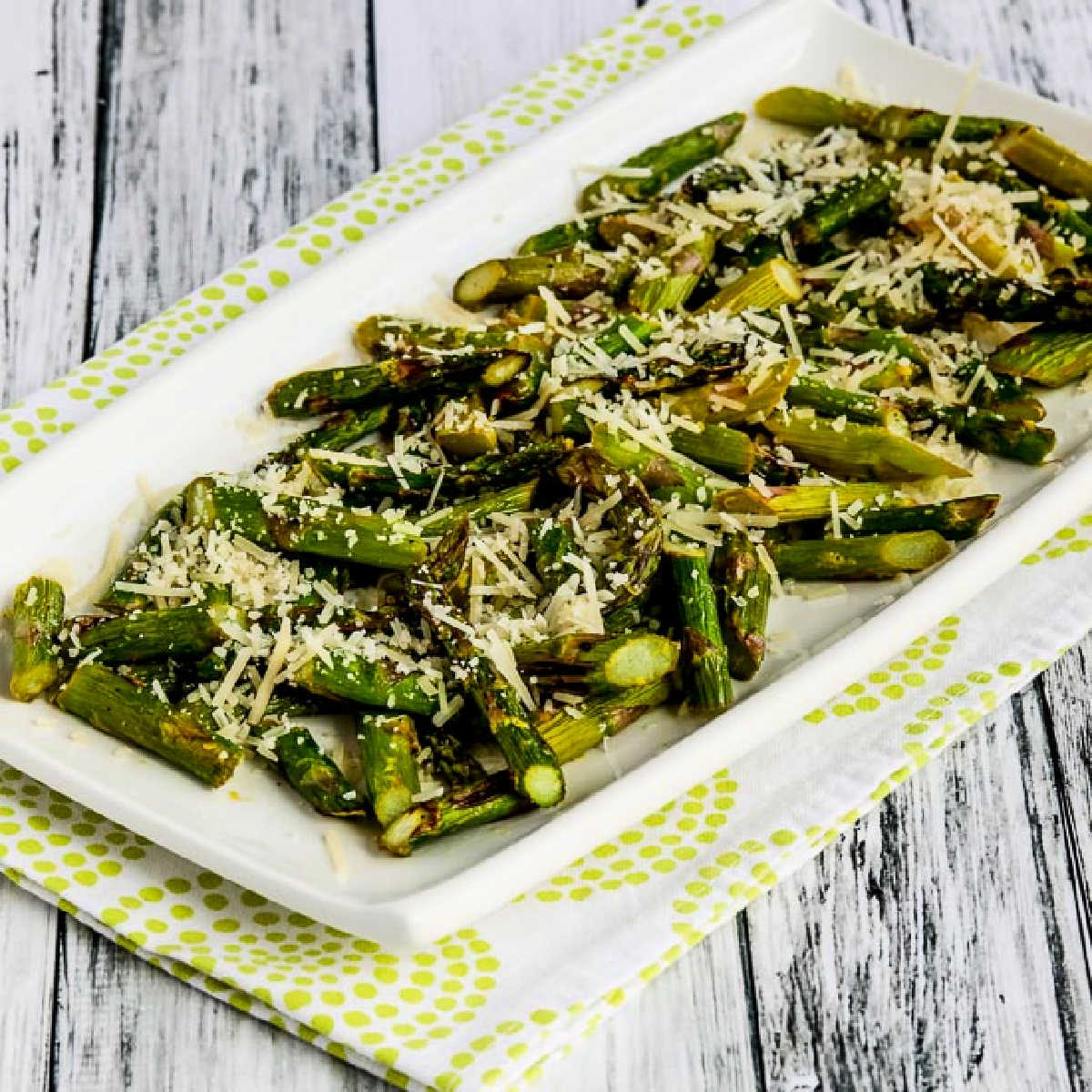 Square image of Air Fryer Asparagus with Lemon and Parmesan on serving platter on green-shite napkin.