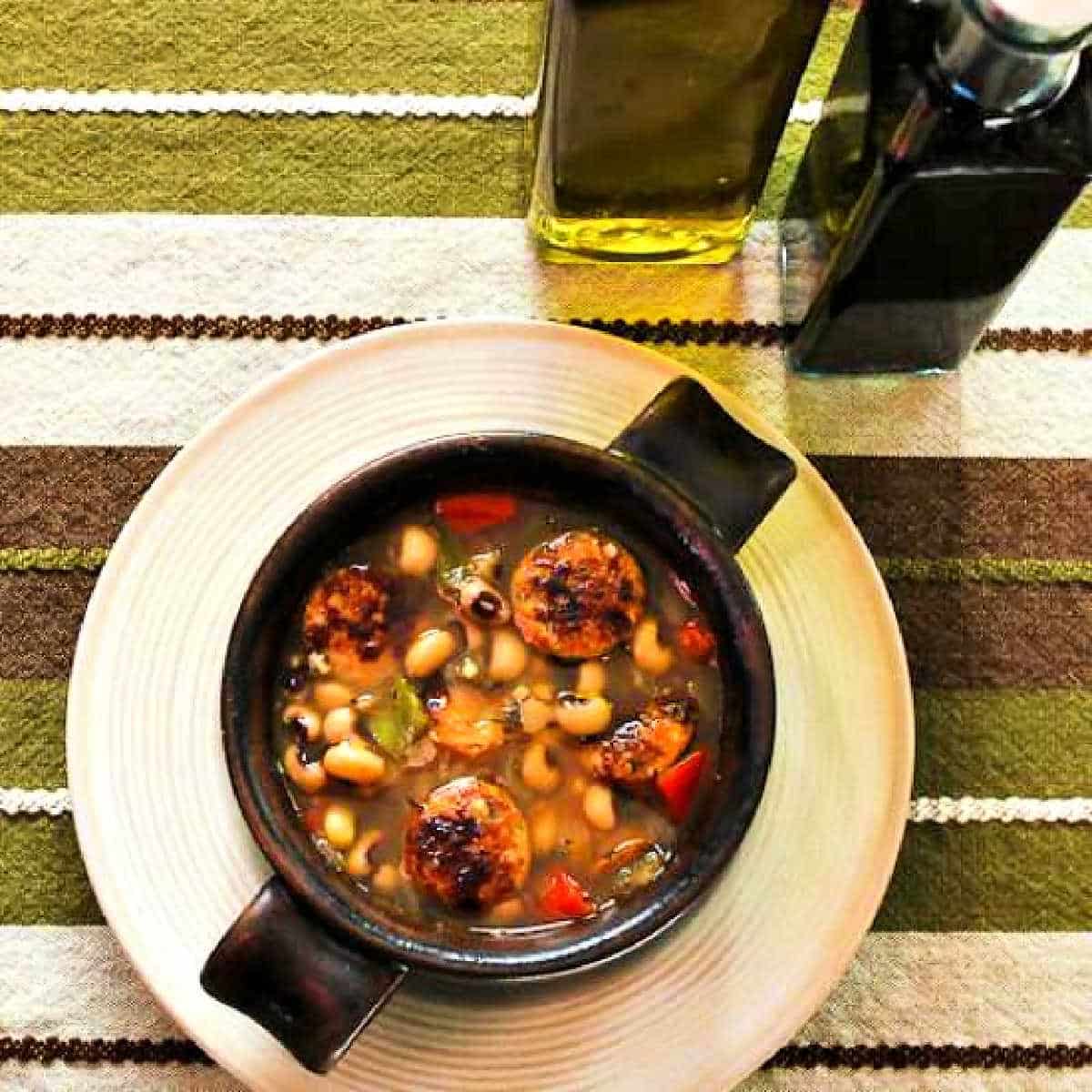 Square image of Black-Eyed Pea Soup shown in bowl with olive oil and sherry vinegar in background.