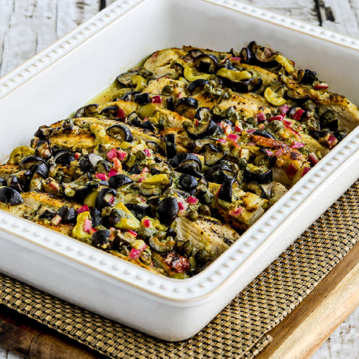 square image of Chicken Bake with Olive and Caper Sauce shown on napkin and cutting board