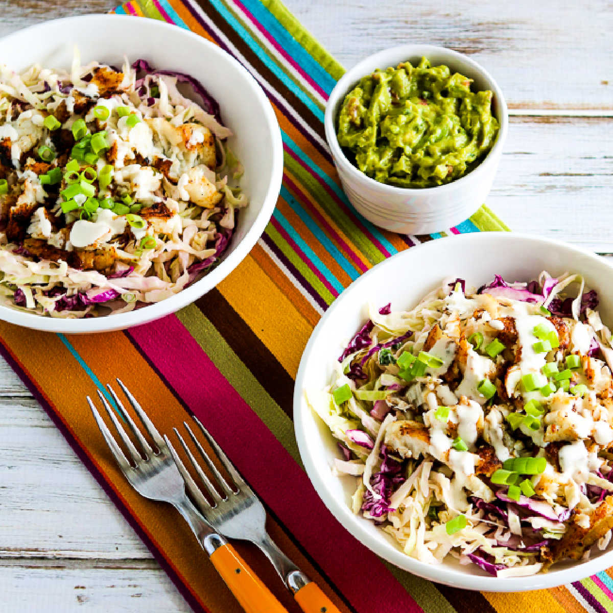 square image of Fish Taco Cabbage Bowls shown on napkins with forks and guacamole