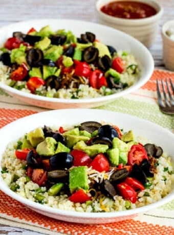 Square image of Ground Beef Cauliflower Rice Taco Bowls shown on napkin with forks and toppings in back.