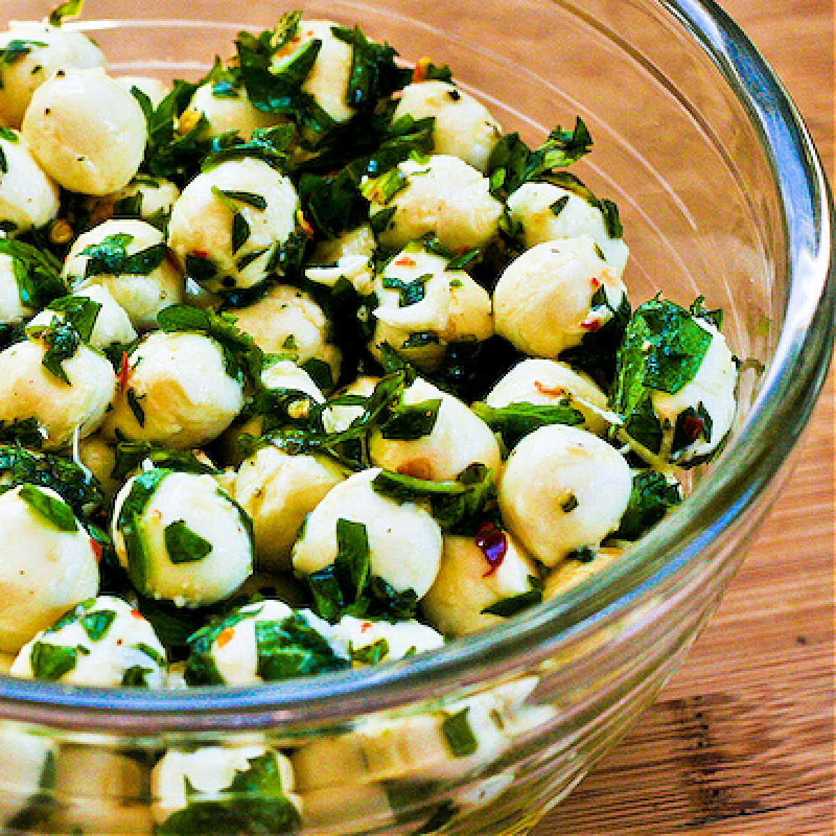 Square image of marinated fresh mozzarella with chopped herbs.