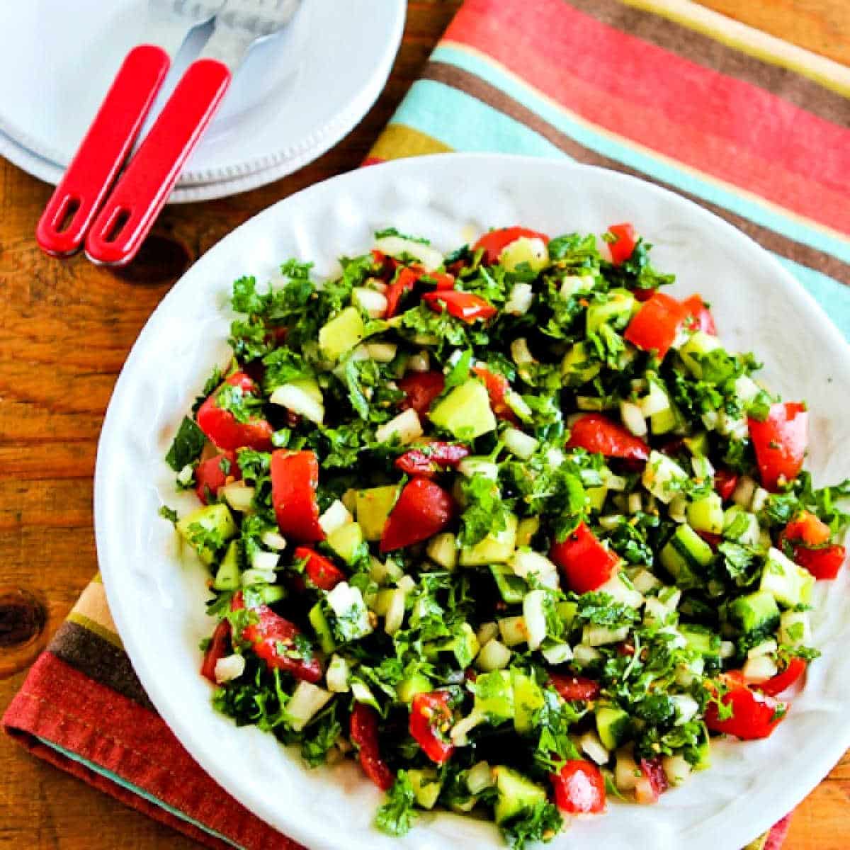 Square image of Middle Eastern Tomato Salad shown in serving bowl with plates and forks on the side.