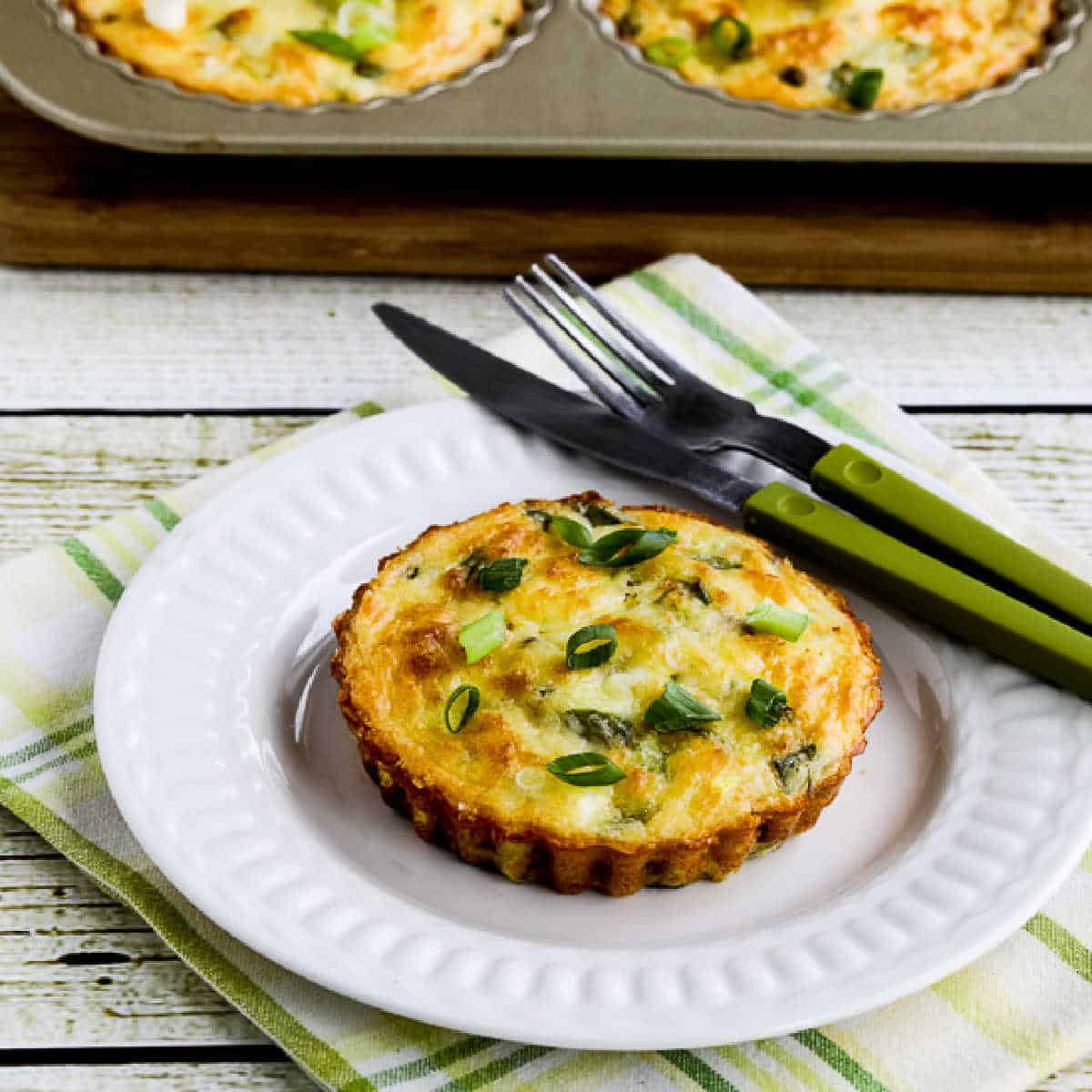 square image of Asparagus Breakfast Tarts with one on plate and tart pan in back