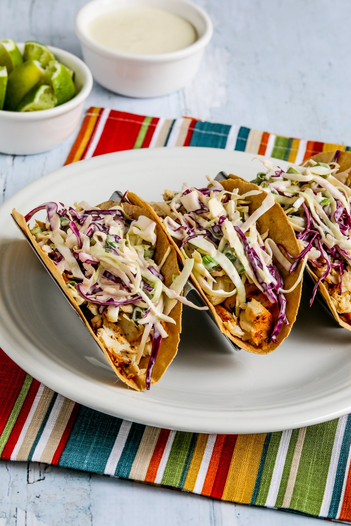 Air Fryer Fish Tacos shown on taco rack with limes and extra sauce in background