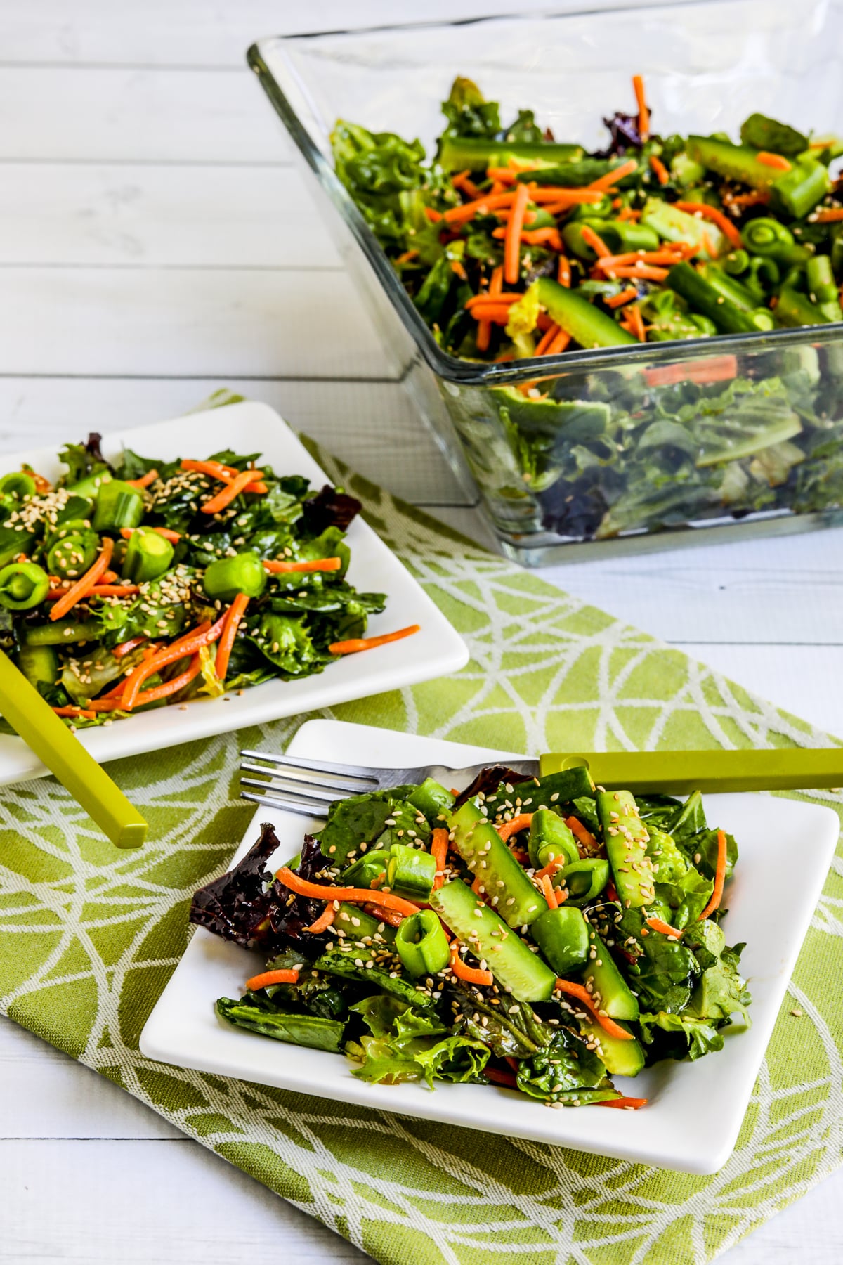 Asian Green Salad with Soy-Sesame Dressing with two serving on square plate and salad bowl in back.