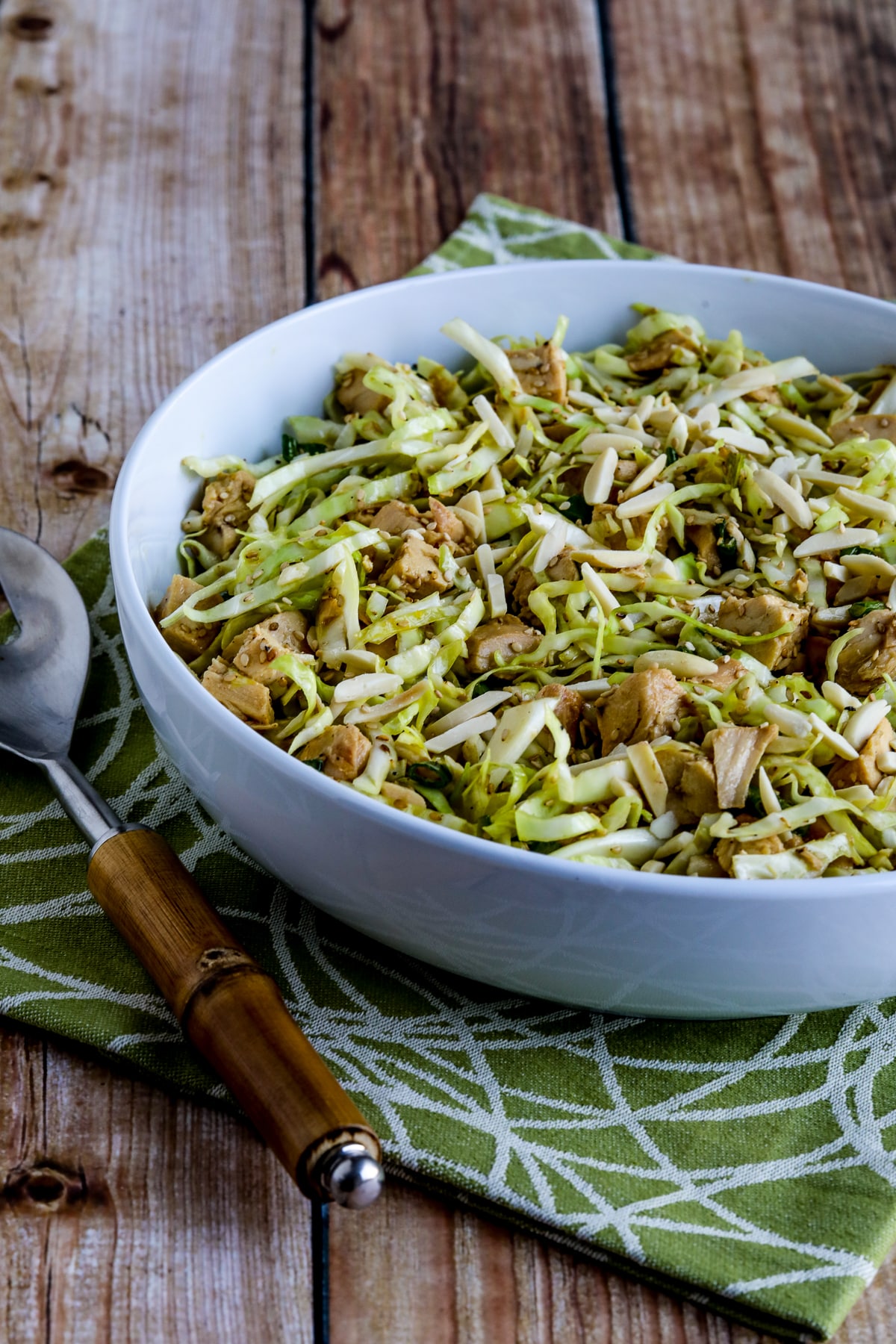 Sandee's Asian Chicken Cabbage Salad in white bowl on green-white napkin with serving fork.