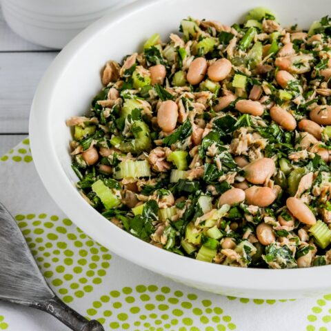 Tuna White Bean Salad shown in serving bowl with salad spoon on green-white napkin.