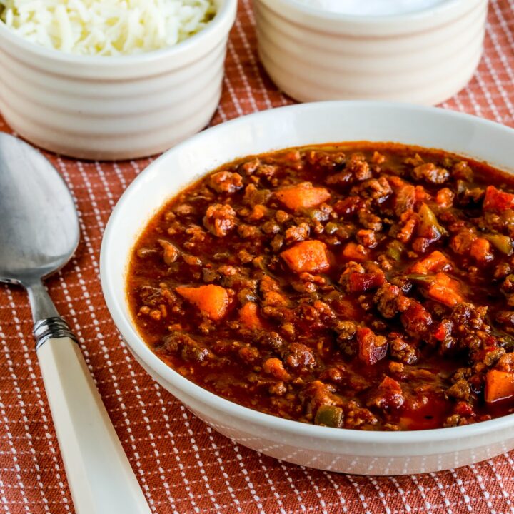 Turkey Sweet Potato Chili shown in serving bowl with spoon, sour cream, and cheese.