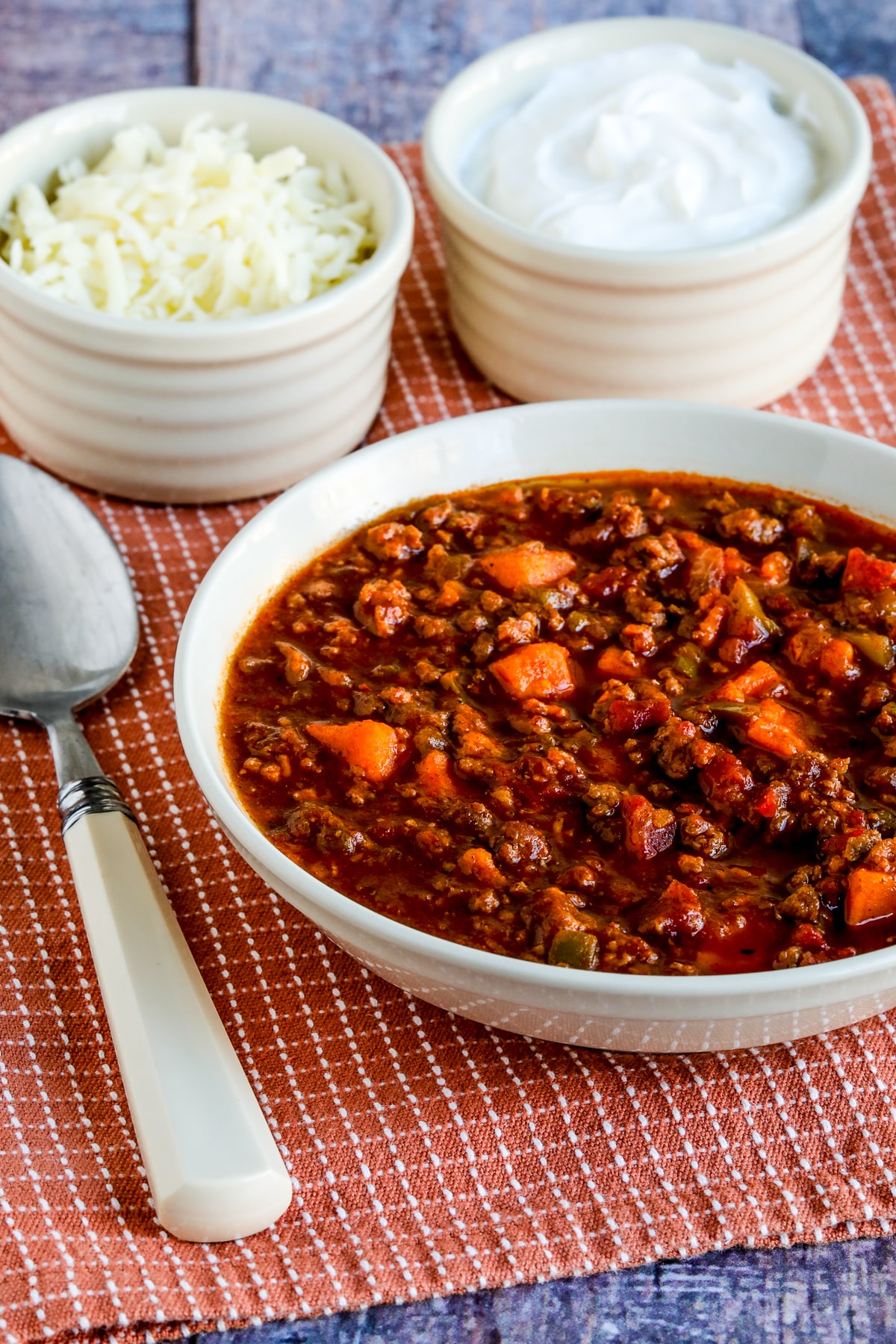 Turkey Sweet Potato Chili shown in serving bowl with spoon, sour cream, and cheese.