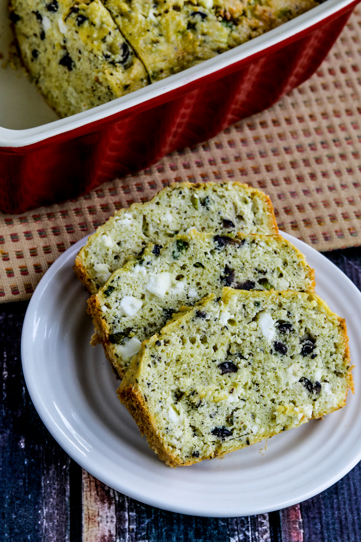 Olive Bread sliced on plate, with rest of loaf in background in baking dish