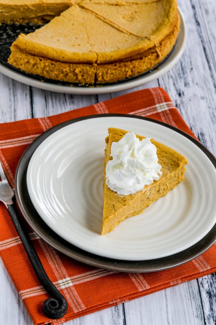 Sugar-Free Pumpkin Cheesecake Pie shown on serving plate with rest of pie on plate in background