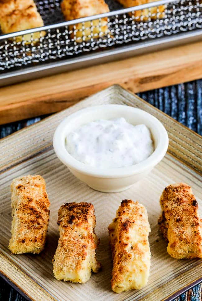 Close-Up photo of Air Fryer Fish Sticks on plate with air fryer basket in background.