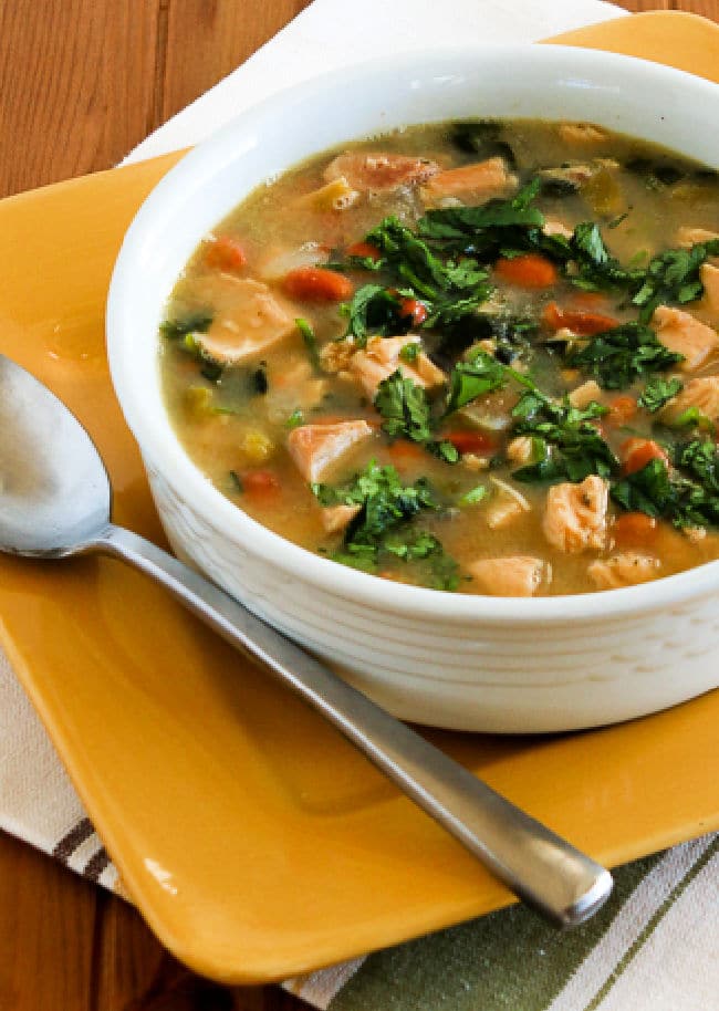 Mexican Chicken Soup show in bowl on yellow plate with spoon, soup garnished with fresh cilantro.