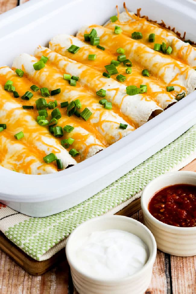 Egg Burritos for a Crowd shown in casserole crock pot with salsa and sour cream in bowls.