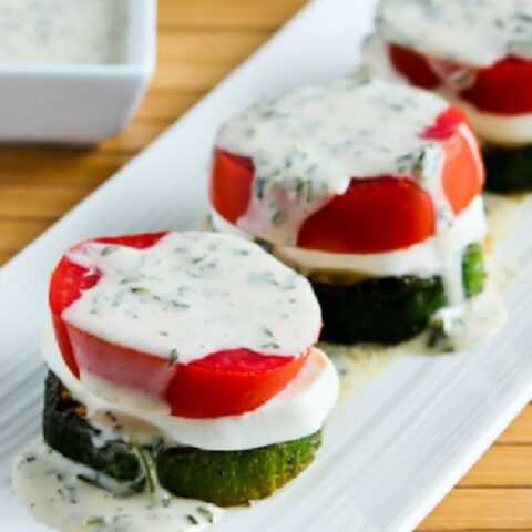 Grilled Zucchini Caprese Stacks on serving plate with basil vinaigrette in background, close-up image